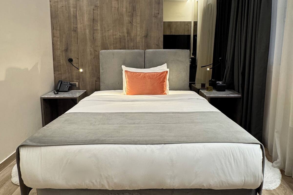 A modern hotel room with a large bed, a wooden accent wall, a bedside table with a phone, and a mirror.