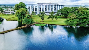 A large hotel with a central courtyard, surrounded by lush greenery and a calm water feature. - Cosmopolitan Condo - Lagoon Centre 701 In the Heart of Hilo (Hilo)