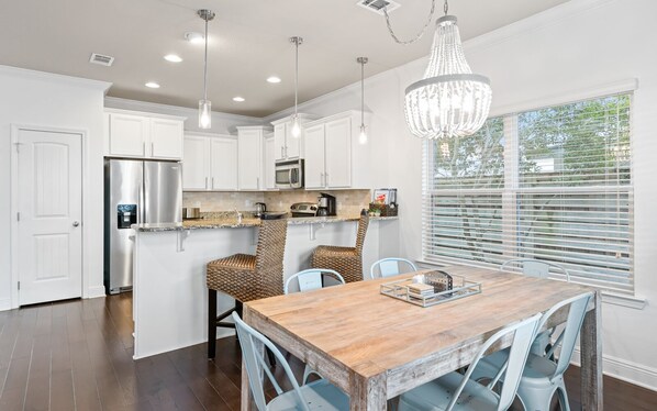 A modern kitchen with white cabinets, stainless steel appliances, and a wooden dining table with chairs.