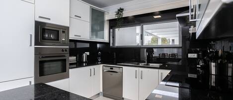 Una cocina moderna con electrodomésticos de acero inoxidable, armarios blancos y encimera de granito negro.