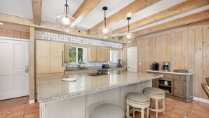A kitchen with wooden beams, a large island with stools, and a coffee maker. - Oceanfront w/ Private Pool & Rooftop Deck | Amazing Views | Sleeps 12 (Jekyll Island)