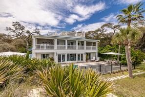 A two-story white building with balconies, surrounded by lush greenery and palm trees.