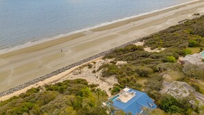 An aerial view of a beach house with a blue roof, surrounded by dense vegetation and a rocky shoreline. - Oceanfront w/ Private Pool & Rooftop Deck | Amazing Views | Sleeps 12 (Jekyll Island)