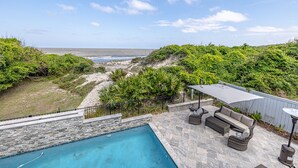 A pool area with a view of the ocean, surrounded by greenery and stone walls. - Oceanfront w/ Private Pool & Rooftop Deck | Amazing Views | Sleeps 12 (Jekyll Island)