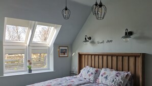 A bedroom with a sloped ceiling, a wooden headboard, a bed with floral bedding, a skylight, and a wall-mounted light fixture.