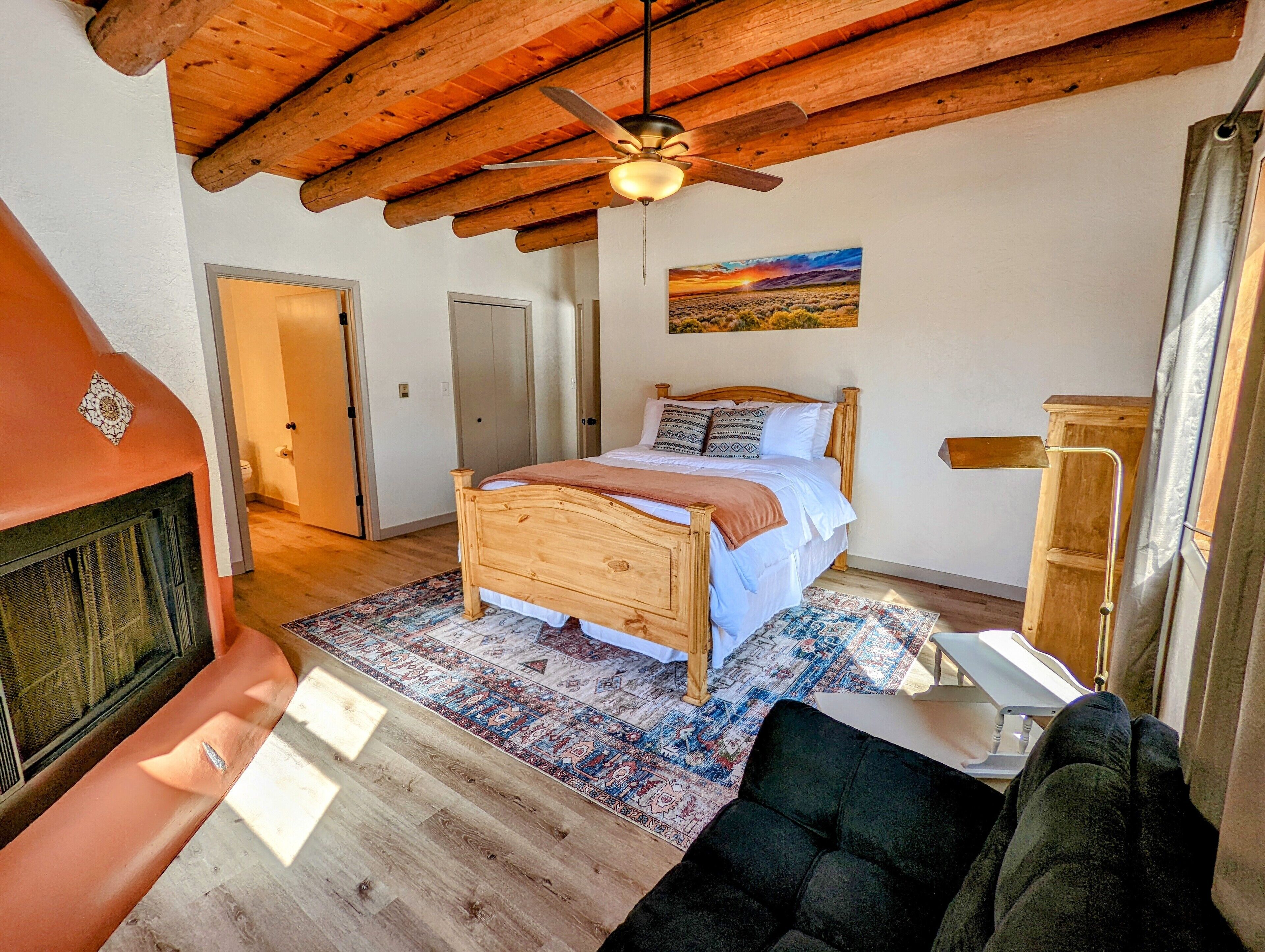 A bedroom with a wooden bed, a ceiling fan, a painting, and a fireplace.