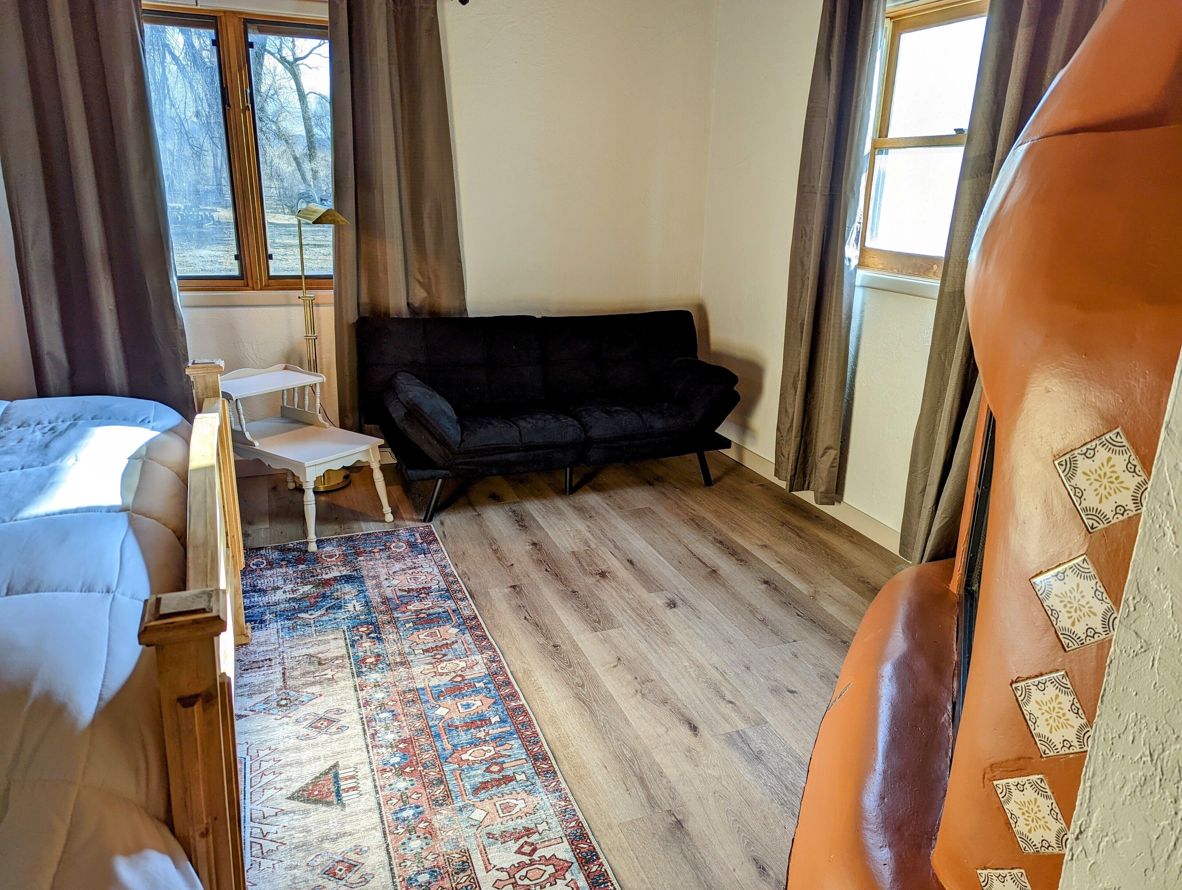 A room with a bed, a black sofa, a small table, and a patterned rug.