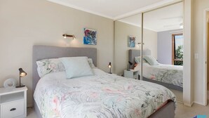 Une chambre à coucher avec un grand lit, des lampes de chevet, une table de chevet, un miroir et des œuvres d’art accrochées aux murs.