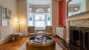Een kamer met een open haard, een ronde tafel met boeken, twee stoelen en een raam met glas-in-lood.