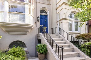 Ein Gebäude mit einer blauen Tür, einer Treppe mit schwarzen Geländern und einem Fenster mit einem verzierten Gitter.