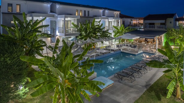 A modern hotel with a swimming pool, outdoor seating, and lush greenery. - Adonis Luxury Village (Kassandra)