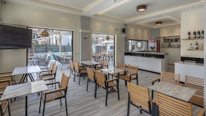 Un restaurant doté de plusieurs tables et chaises, d’un espace cuisine et offrant une vue sur l’extérieur.