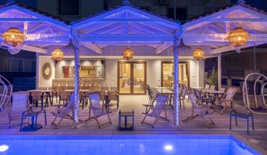 Ein Poolbereich mit Liegestühlen und Sonnenschirmen, eine Bar und ein Restaurant mit Blick auf den Pool.