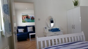 A bedroom with a bed, a dresser, a mirror, a blue sofa, and a painting of a coastal scene.