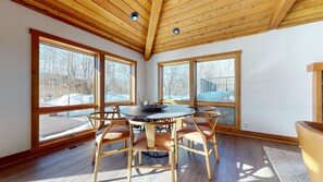 A room with a wooden ceiling, large windows, a round table with chairs, and a view of a snowy landscape. - Snowcreek VII 1403 Deluxe Townhouse, Stunning Mountain Views, 2 Car Garage, Washer Dryer by RedAwning (Mammoth Lakes)