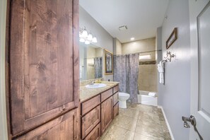 A bathroom with a wooden vanity, a sink, a mirror, a toilet, a bathtub, and a shower curtain. - Hillside River Retreat Rg 306 3 Bedroom Condo by RedAwning (New Braunfels)