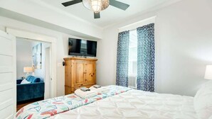 Une chambre d’hôtel équipée d’un lit, d’une télévision, d’une armoire et d’une fenêtre avec des rideaux à motifs.