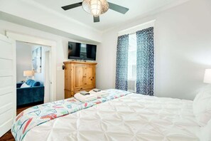 A hotel room with a bed, a television, a wardrobe, and a window with patterned curtains.