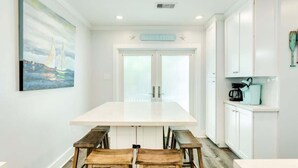 Une cuisine moderne avec des meubles blancs, un îlot central doté de bancs et un tableau représentant des voiliers accroché au mur.