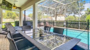 Un espace extérieur abrité, doté d'une table en verre et de chaises en osier, donnant sur une piscine.
