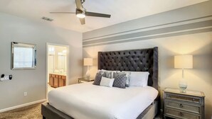 Une chambre avec un grand lit, un ventilateur de plafond, une table de chevet avec une lampe et une commode.