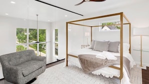 Ein modernes Schlafzimmer mit Himmelbett, einer Couch und Blick auf Grün.