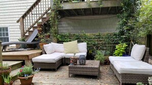 A wooden deck with wicker furniture, including a sofa and a chair, surrounded by potted plants. - CB House (Bike Trail, Brewery, Boardwalk, Park) (Carolina Beach)
