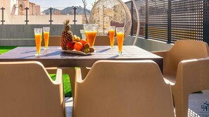 Una mesa con frutero y vasos de jugo de naranja, con asientos al aire libre y vista a la ciudad.