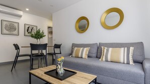 Un salón moderno con un sofá gris, dos sillas negras, una mesa de centro con un florero y dos espejos dorados en la pared.