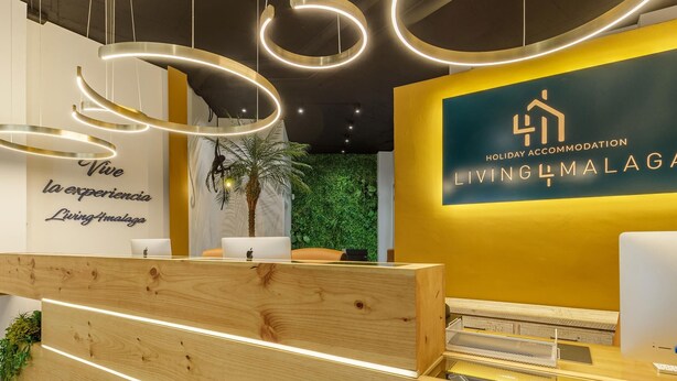Una recepción con frente de madera, una pared con jardín vertical y un letrero que dice "Holiday Accommodation Living4Malaga".