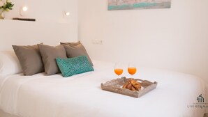 A neatly made bed with pillows, a tray with croissants and juice glasses, and a painting on the wall.