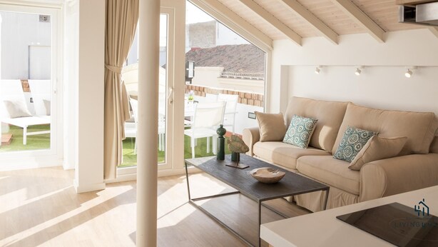 A spacious living room with a high ceiling, large windows, a beige sofa, and a coffee table.