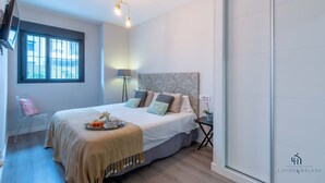 A modern bedroom with a large bed, a bedside table, a floor lamp, and a window with blinds.