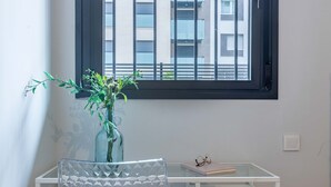A room with a window, a vase with plants, a chair, and a table with a book and glasses.