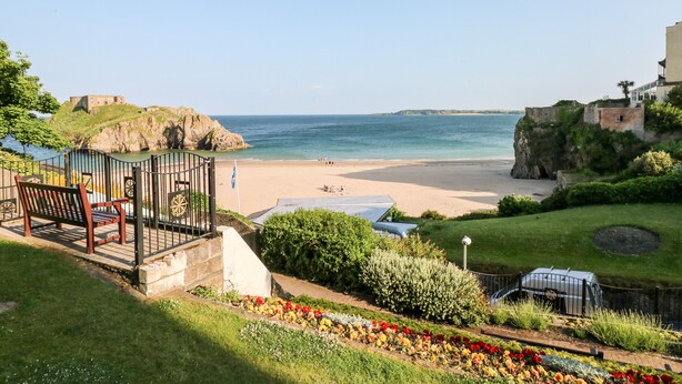 A coastal view with a beach, a historic building, and a garden with flowers. - Ty Cwtch (Tenby)