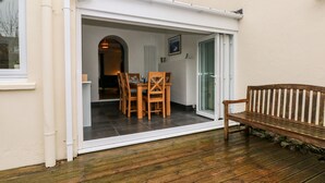 A covered patio with a wooden table and chairs, a bench, and a sliding glass door leading to an interior space. - Ty Cwtch (Tenby)