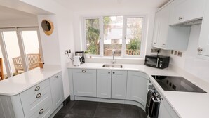 A modern kitchen with white cabinets, a built-in microwave, and a window with a view of the outside. - Ty Cwtch (Tenby)