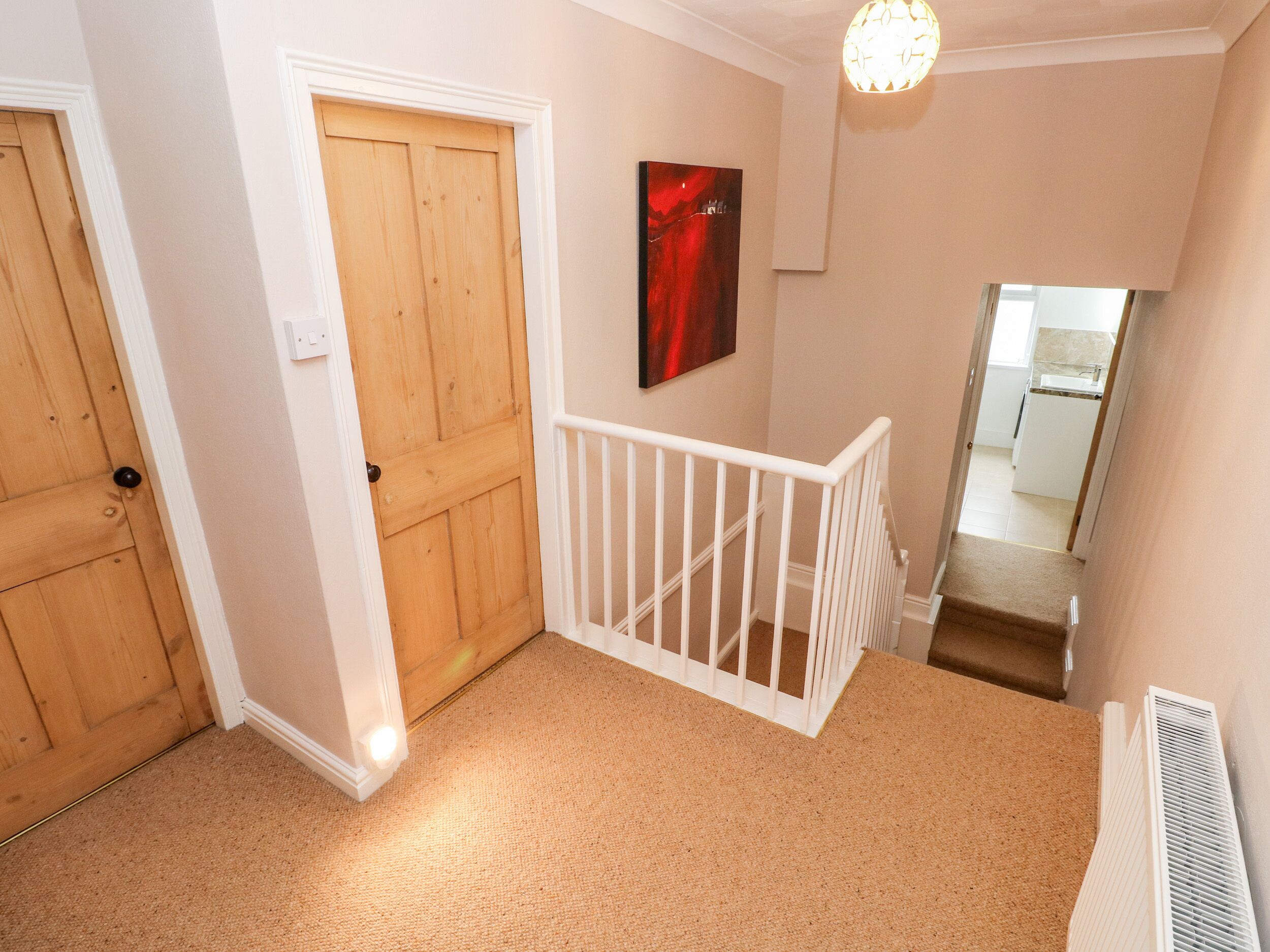 A hallway with a wooden door, a white railing, a red abstract painting, and a view into a kitchen.