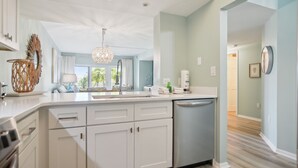 A modern kitchen with white cabinetry, a built-in dishwasher, and a large island with a sink. There is a decorative hanging light fixture above the island. - 237 Shorewood Villas - Ocean Views - Exceptional Update - Discounted Rates! (Hilton Head Island)