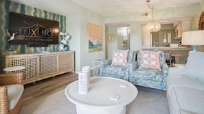 A modern living room with a sofa set, a coffee table, and a wooden console. A sign for 'LUXURY Rentals of Hilton Head' is visible on the wall.