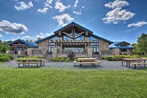 A lodge with a stone facade, a covered patio area, and picnic tables in the foreground. - Chalet in the heart of Poconos, romantic getaway near pools and lake (Arrowhead lake)