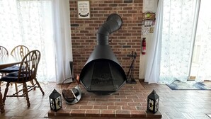 Een kamer met een schouw van baksteen, houten vloeren, een klok en een eethoek met stoelen.