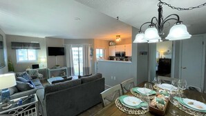 A living room with a sofa, dining table set for a meal, and a kitchen in the background. - Flip Flop O'Clock-Gulf Views • 6 Pools • Beachfront Resort Escape (Gulf Shores)