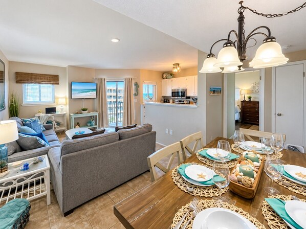 A modern living room with a sofa, dining table set for four, and a kitchen area with appliances.