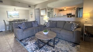 A living room with a gray sectional sofa, a round coffee table with a plant, and a large mirror above the sofa. - Flip Flop O'Clock-Gulf Views • 6 Pools • Beachfront Resort Escape (Gulf Shores)