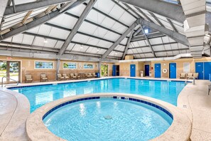 Una piscina interior con techo transparente, varias entradas y sillones de descanso alrededor del borde.