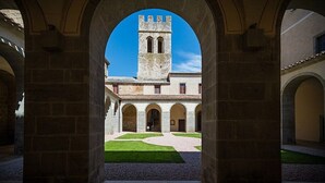 Un corredor arqueado con vistas a un edificio que cuenta con una torre y un patio con piso estampado.