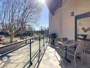 A balcony with a table and chairs, overlooking a river with boats and trees. - View of the Canal du Midi - Comfortable apartment for 6 people (La Redorte)