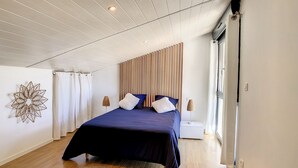 Un dormitorio con una cama grande, suelo de madera, un adorno en la pared y una ventana con cortinas.