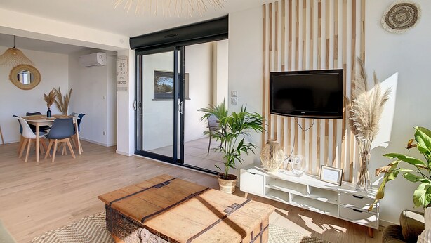 Una sala moderna con una mesa de centro de madera, un televisor de pantalla plana montado en una pared de madera, y un área de comedor con una mesa redonda y sillas.